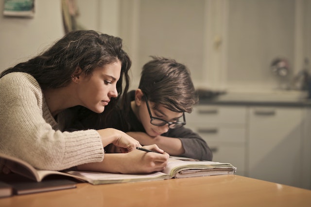 A young woman helps a younger boy with homework. Sometimes selfless sacrifices are as small as this!