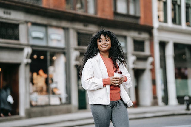 A young woman of color takes a walk with a cup of coffee in hand.