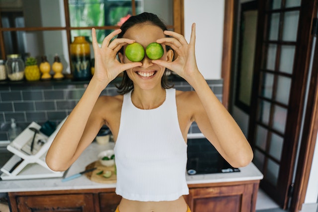 Meal planning and cooking are fun! A young woman plays with cucumber slices, using them as glasses, while she cooks.