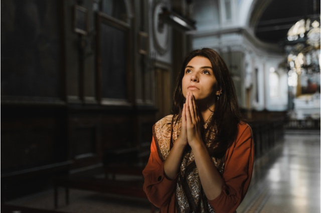 A young Latina woman prays in a large cathedral.